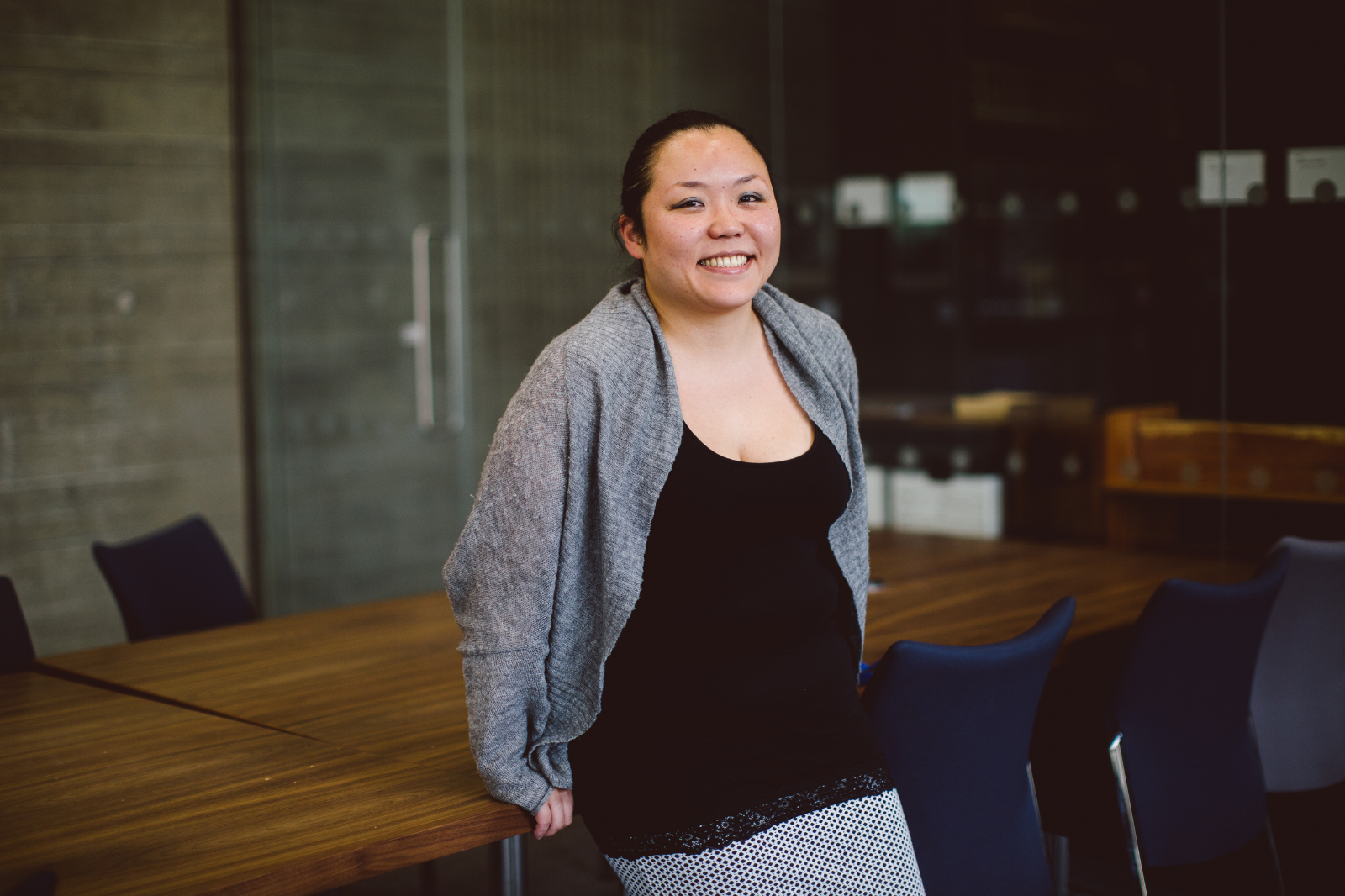 Professional woman stands in board room, smiling to camera. 