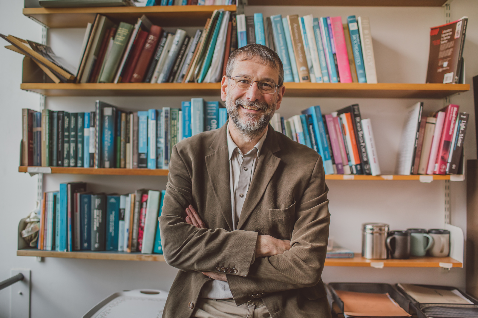 Man, smiling, looking to camera, standing in front of a large bookshelf