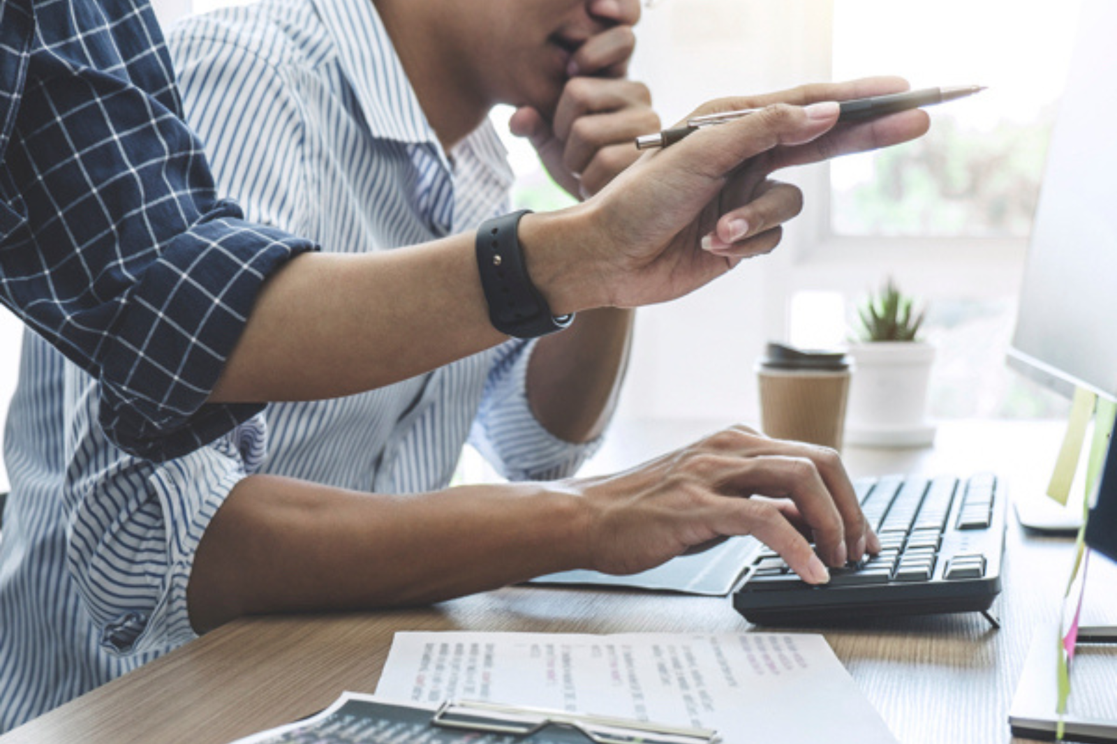 Close up of two individuals working at a desk and computer