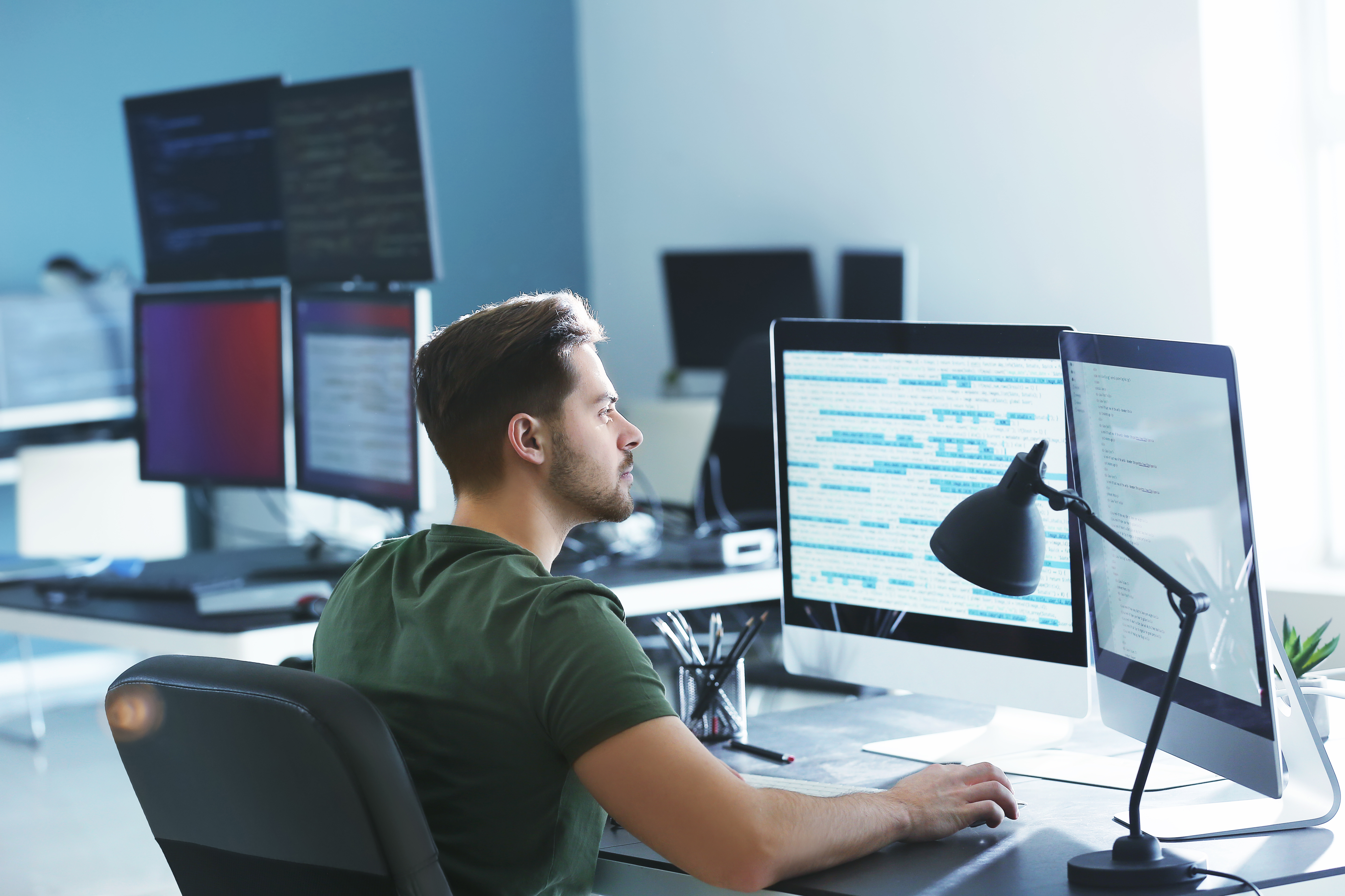 Man sits at desk working over two screens.
