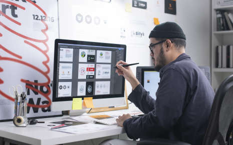 Graphic designer sitting at a desk drawing on his Apple computer.