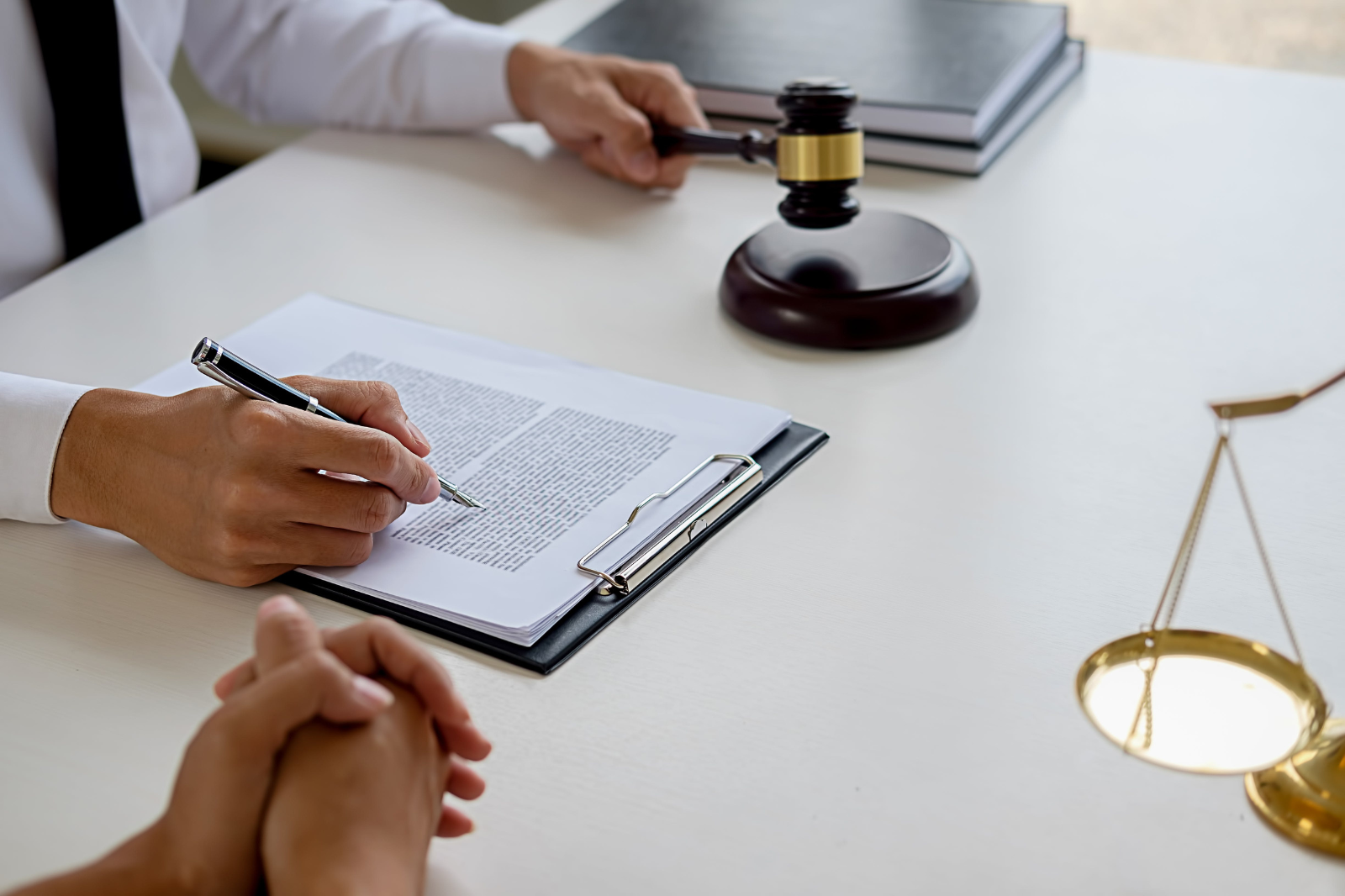 Close up of a person signing a contract holding a gavel, next to a pair of scales. 