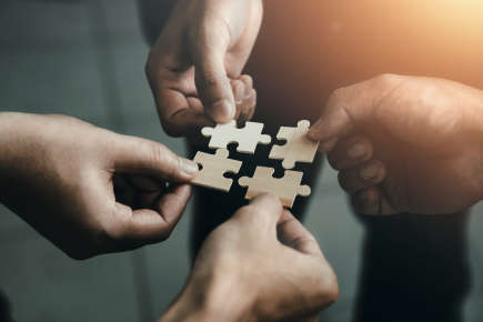 Abstract image of four hands holding jigsaw pieces
