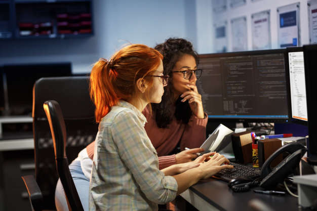 Two women software engineers looking at the coding on their computer screen.