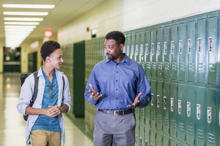 High school student and his teacher talk while walking down a school hallway.