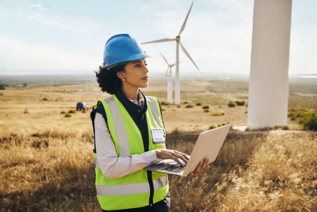 Windmill on farm, black woman in clean energy typing on laptop and electricity generation with wind turbines in Africa.