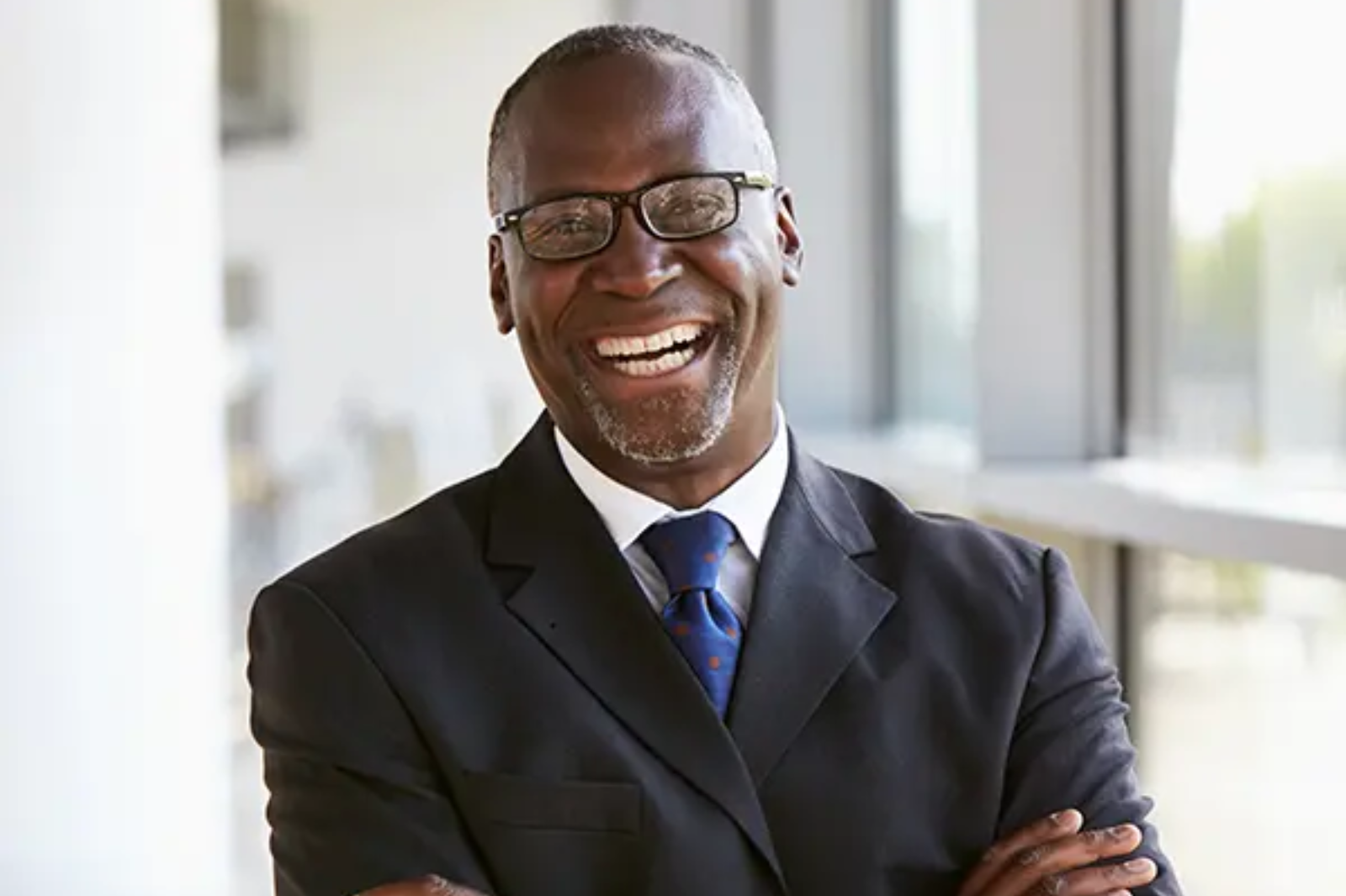 Man in suits stands looking to camera, smiling. 