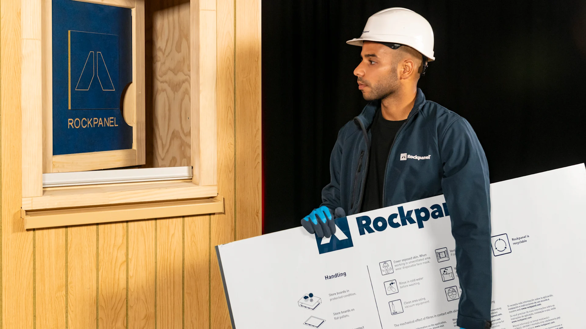 Mand bærer Rockpanel plade for at montere den på facade ved vindue.