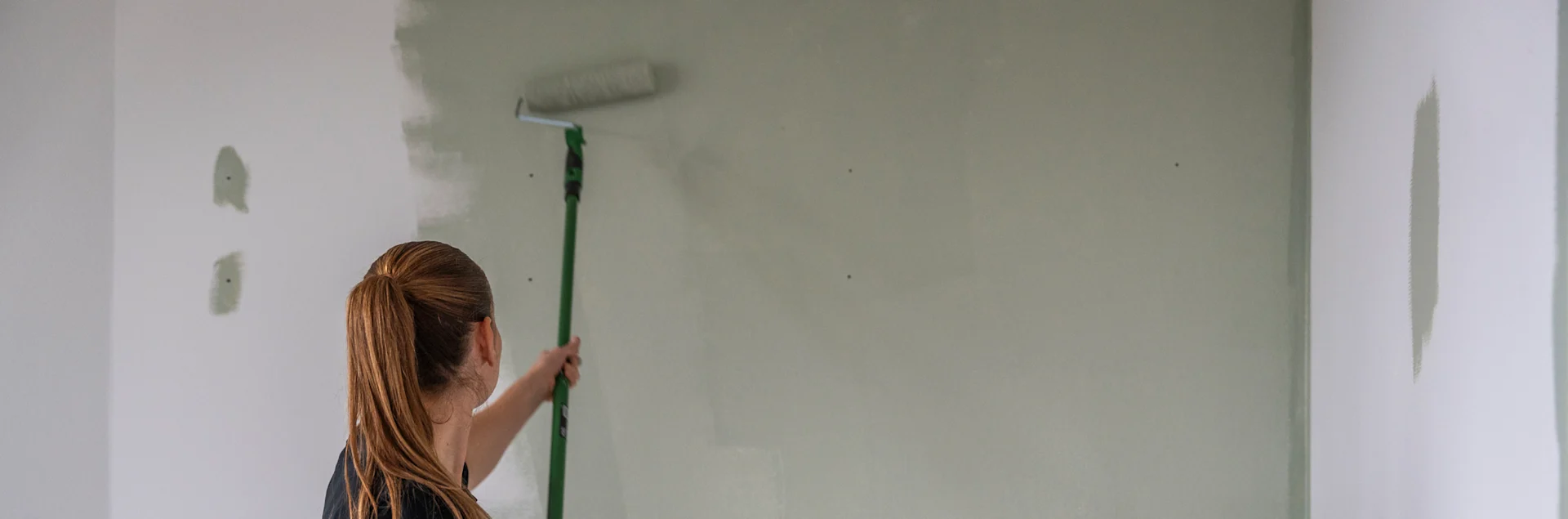 Kvinde maler grøn farve på en hvid væg.
