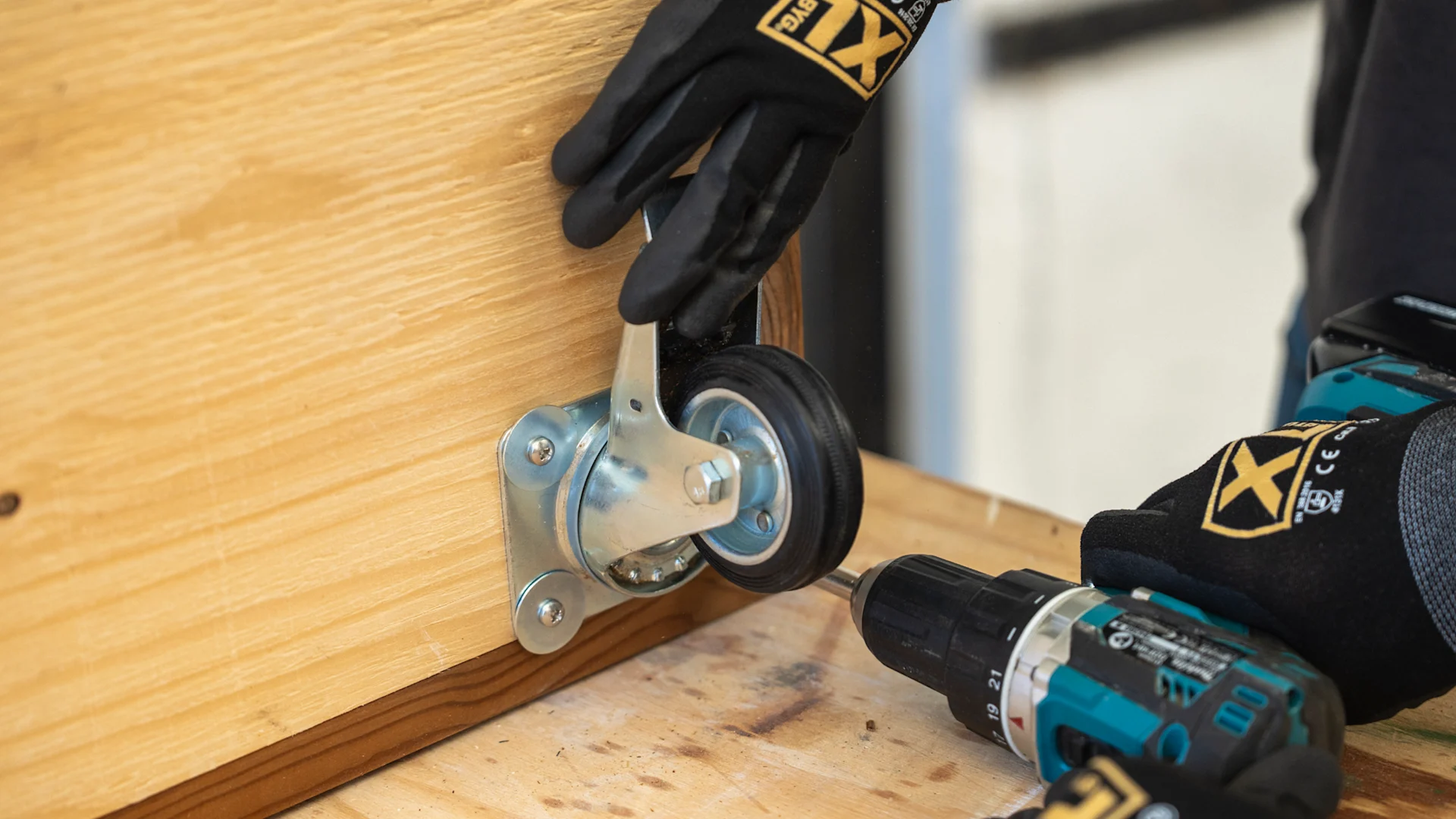 Der monteres møbelhjul med skruemaskine af en person iført XL-BYG handsker.