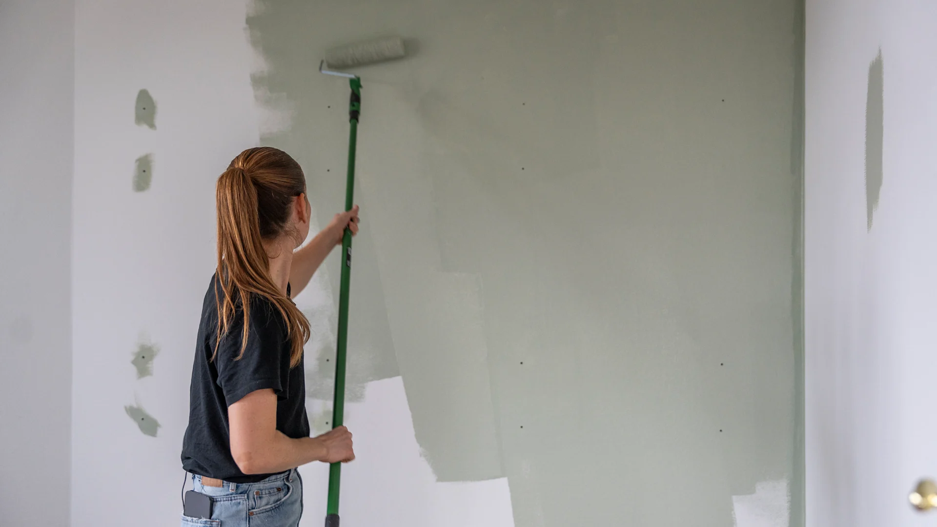 Kvinde maler grøn farve på en hvid væg.