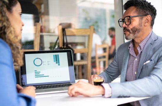 Two individuals discussing graphs shown on laptop screen