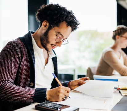 Individual at desk with calculator and pen reviewing paperwork