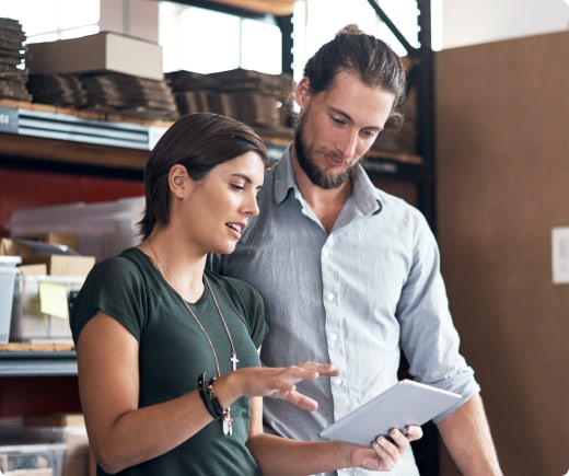 Two individuals in a warehouse looking at a tablet