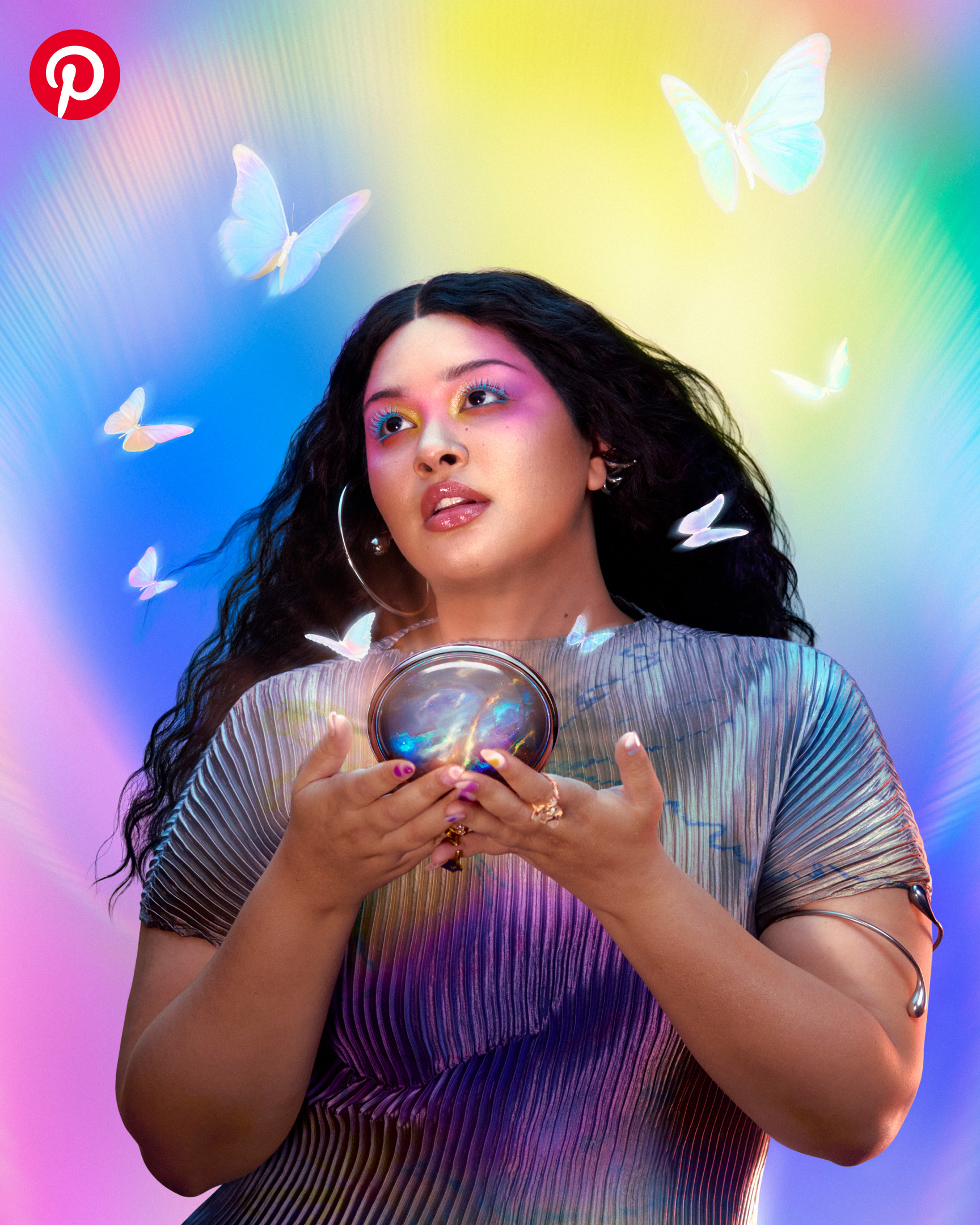 A woman with long, windswept hair wearing colorful makeup and holding a gold compact