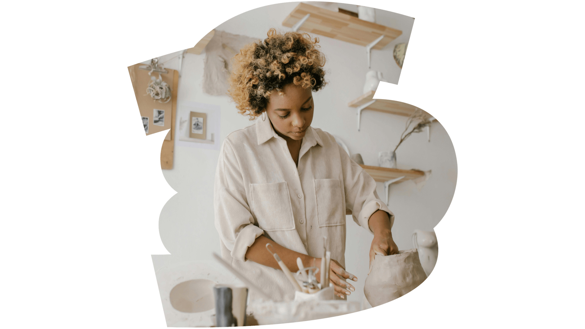 A woman in a pottery studio uses her hands to shape a clay vase