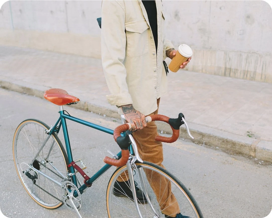 A man holding a cup of coffee walks his bike down a city street