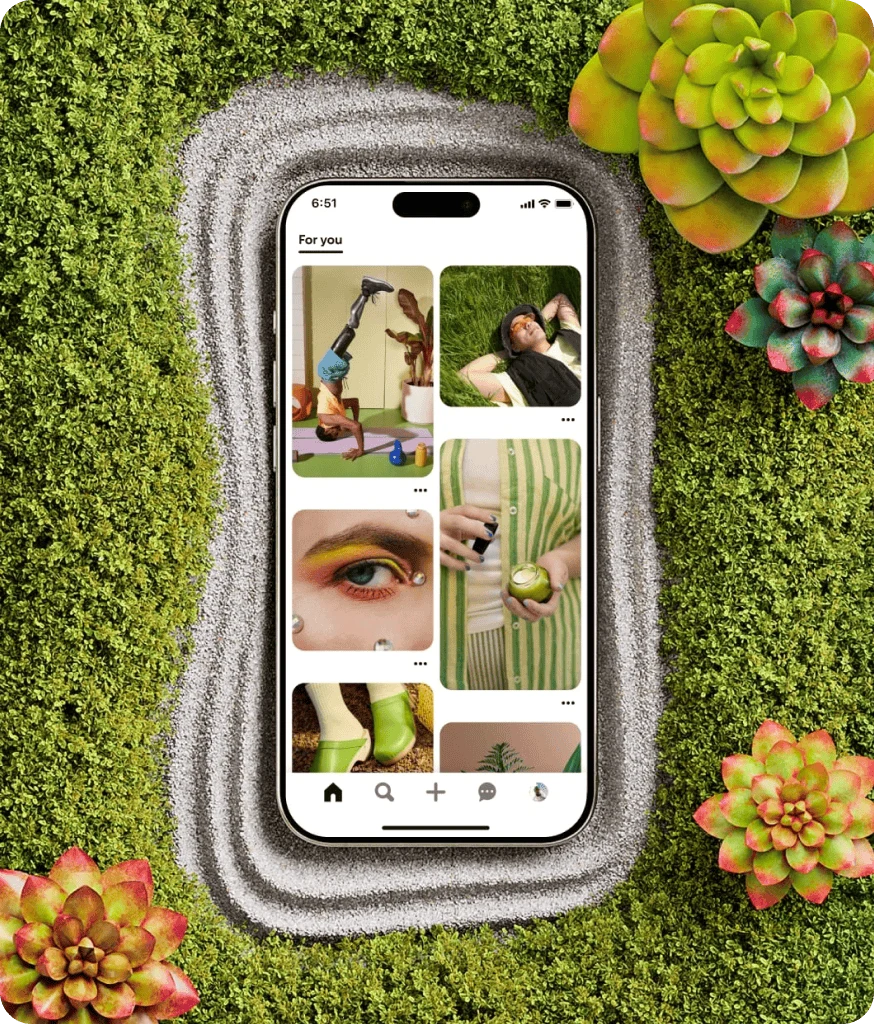 A smartphone is nestled within a field of grass with colourful succulents surrounding it. The phone screen shows the Pinterest app.