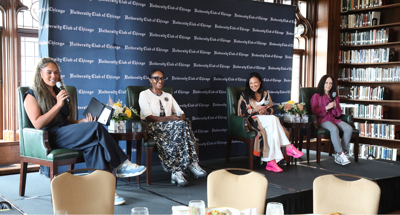 Four people sit on a stage in front of a sign that reads “University Club of Chicago.”