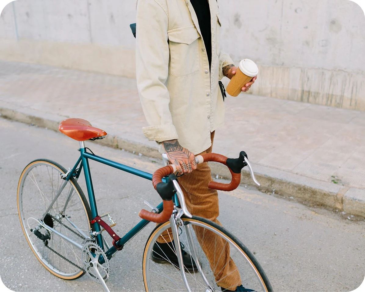 A person walks with a bike while carrying a coffee cup.