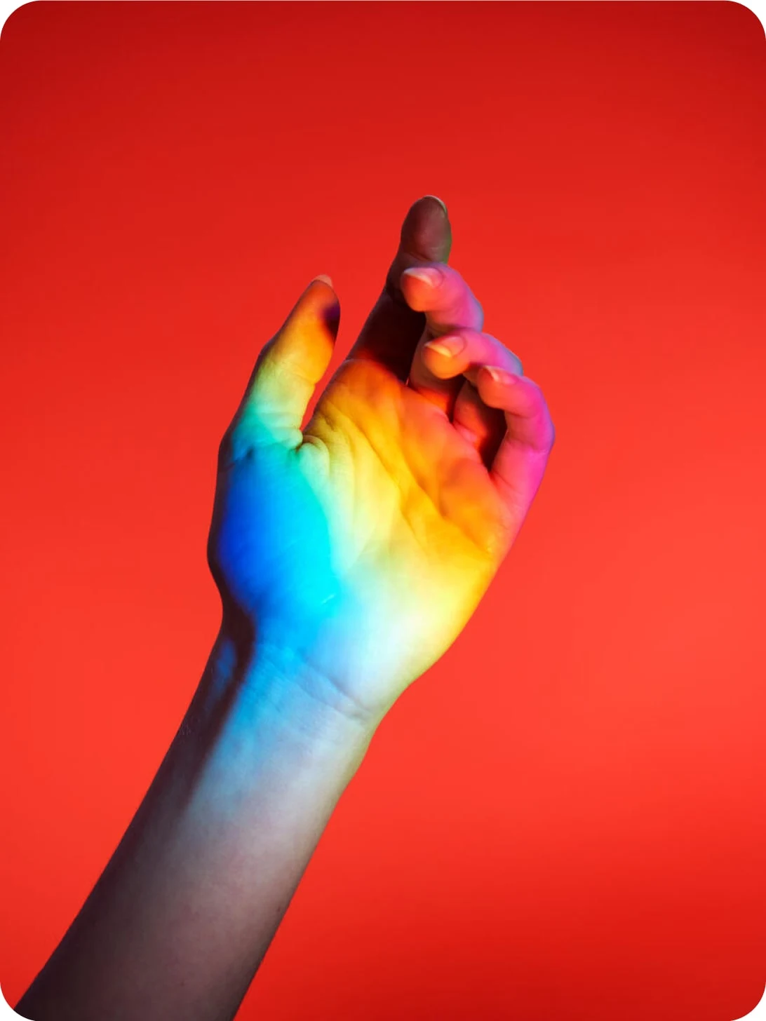 A rainbow is projected onto a raised hand against a red background