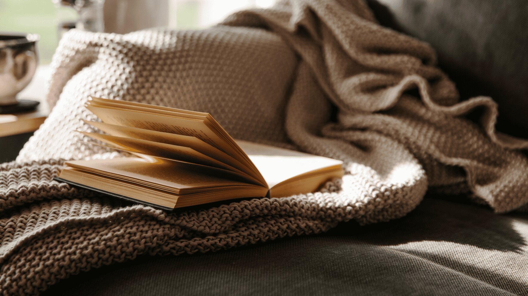 Ein aufgeschlagenes Buch auf einer gemütlichen Strickdecke, ein Sinnbild für die Behaglichkeit und Ruhe eines kleinen Leseplatzes.