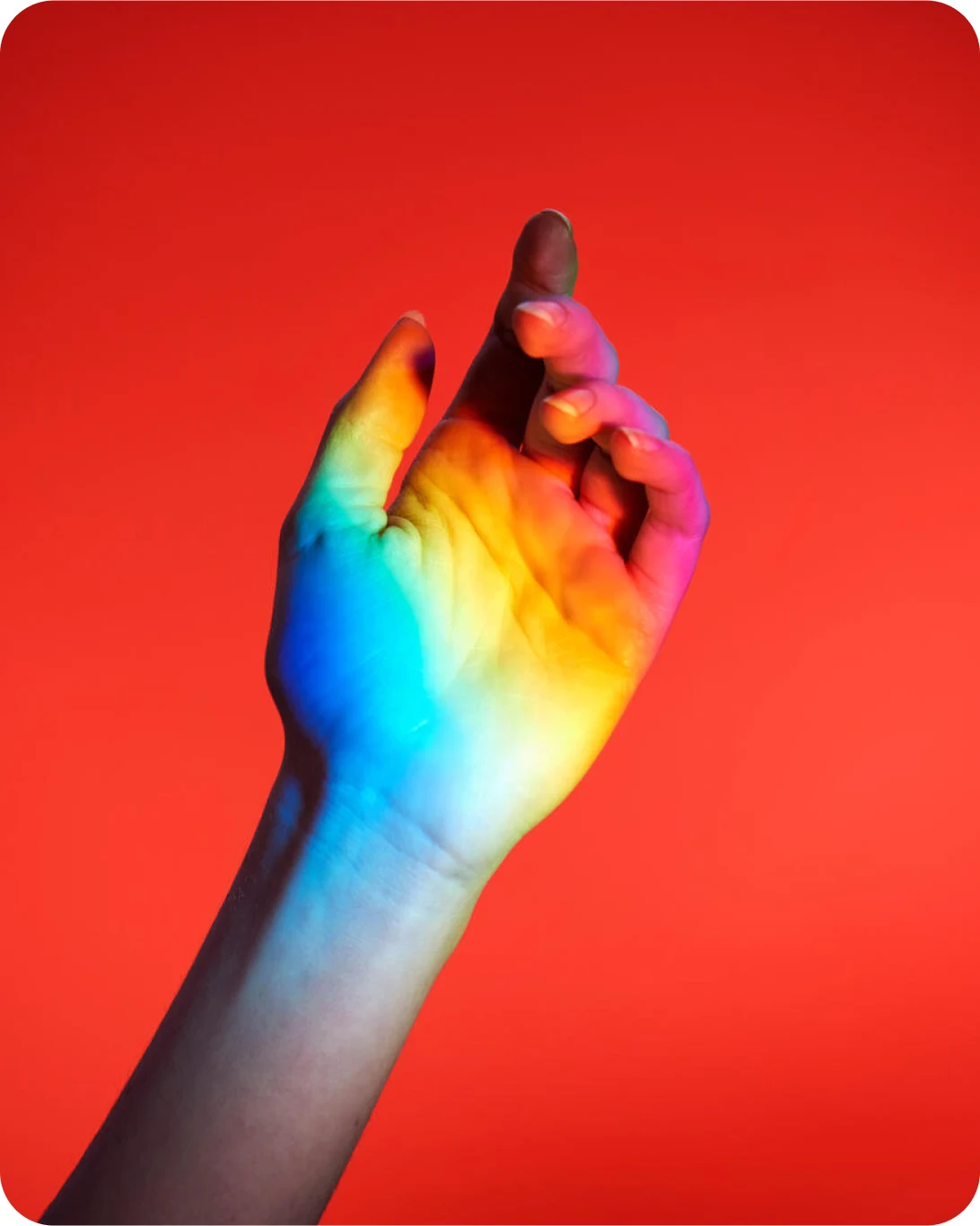 Over a red background, a raised hand is illuminated in a rainbow