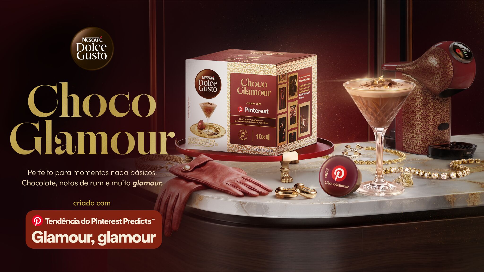 Caixa e máquina  NESCAFÉ® Dolce Gusto® Choco Glamour com bebida de chocolate, joias, anéis e luvas vermelhas sobre mesa de mármore.
