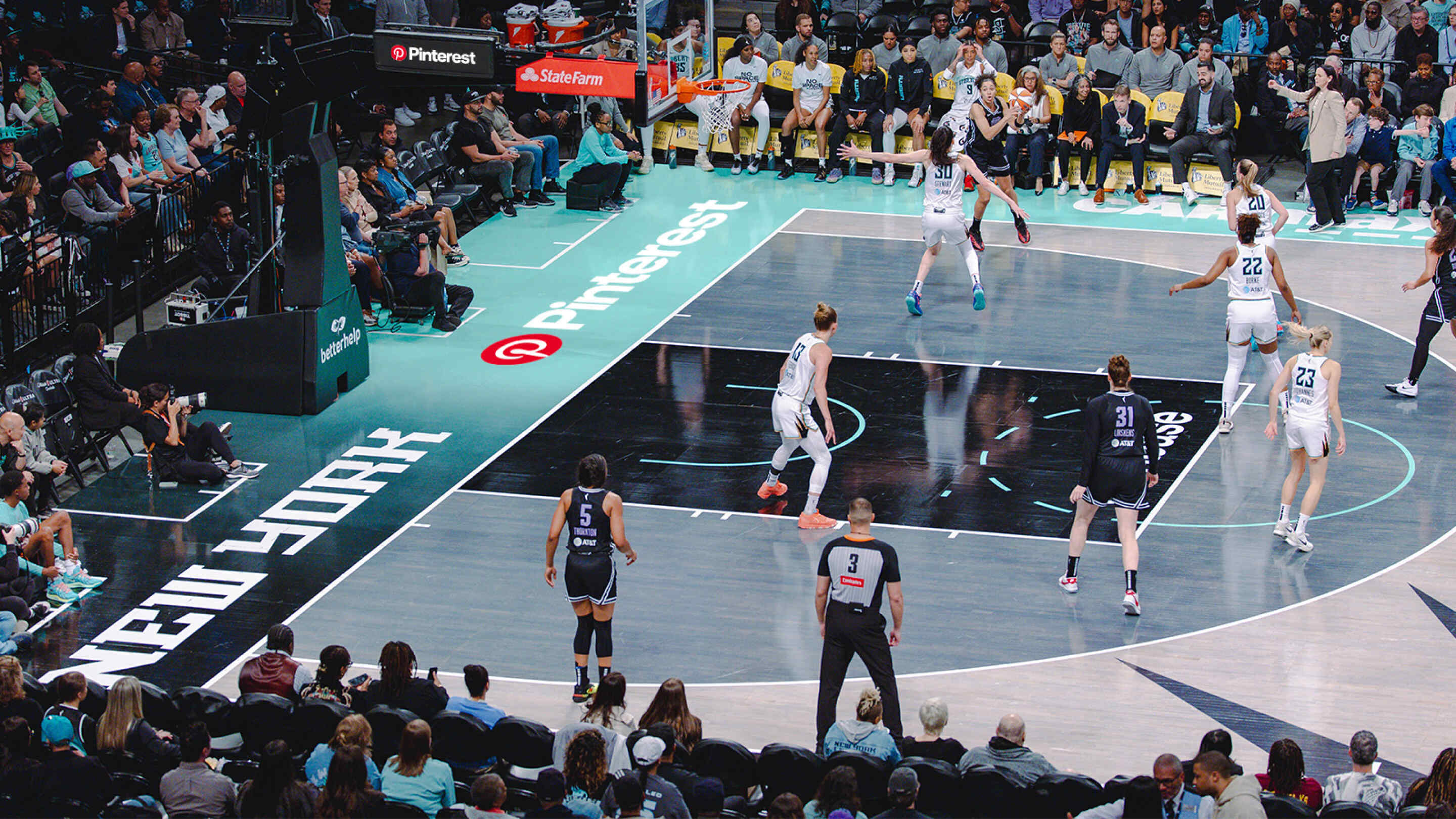 The New York Liberty WNBA team plays basketball on their home court. The Pinterest logo is painted on the sideline.
