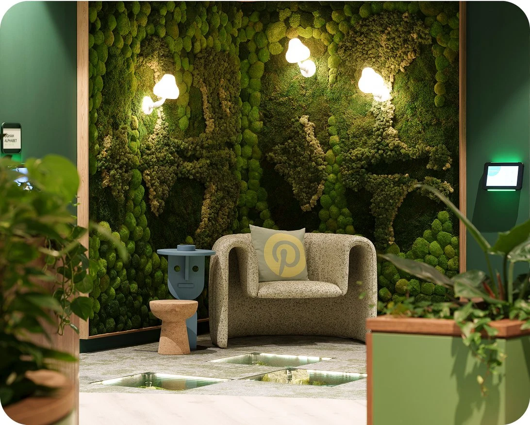 A beige armchair with a pillow that has the Pinterest logo printed on it is surrounded by vegetative office decor.