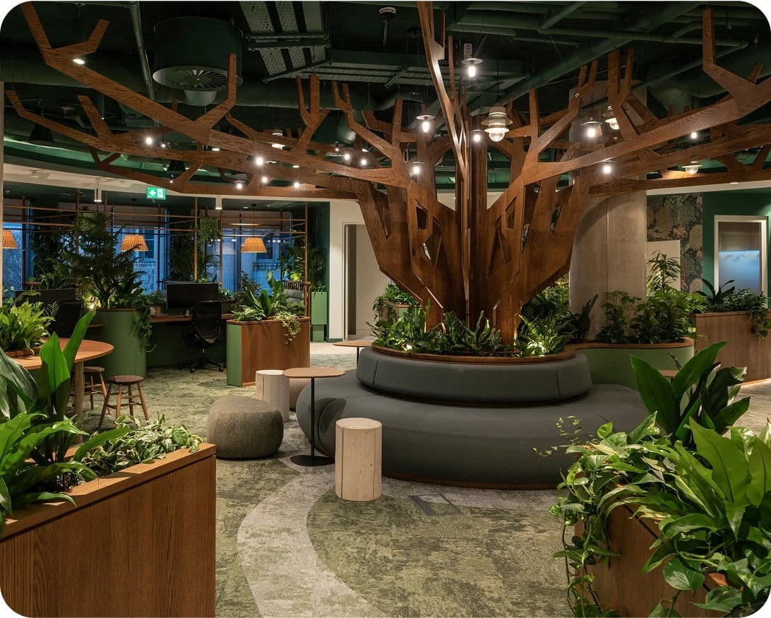 An office space with a lot of plants and a large wooden tree sculpture.