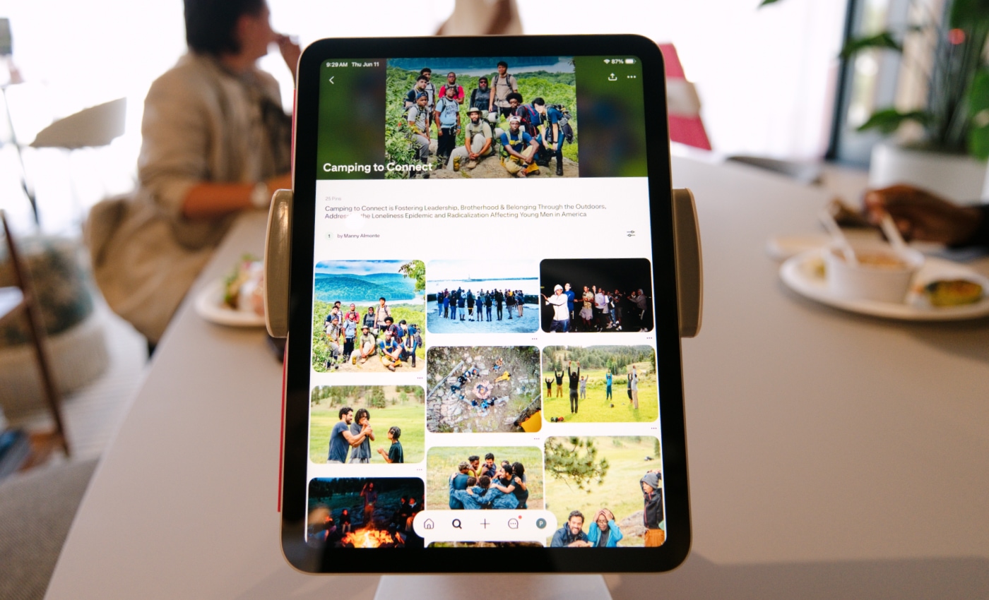 Tablet on a cafe table displaying a Pinterest board titled “Camping to Connect,” with blurred people eating at the table in the background. 