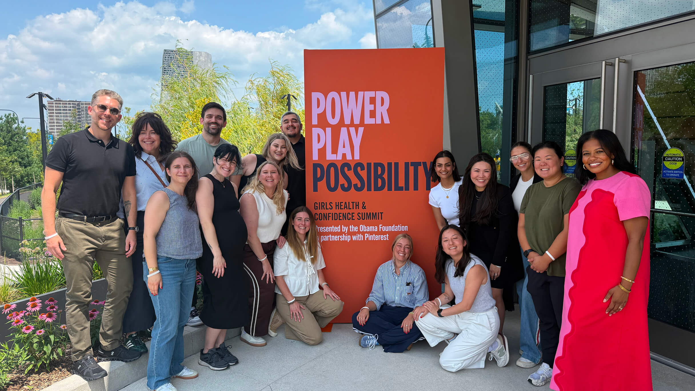 A group of people stand outside an office building in front of a sign that reads “Power Play Possibility." 