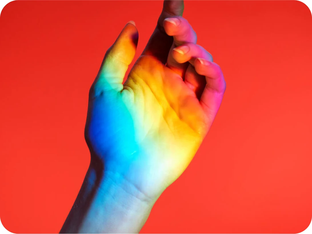 A hand against a red background has rainbow light shining on it.
