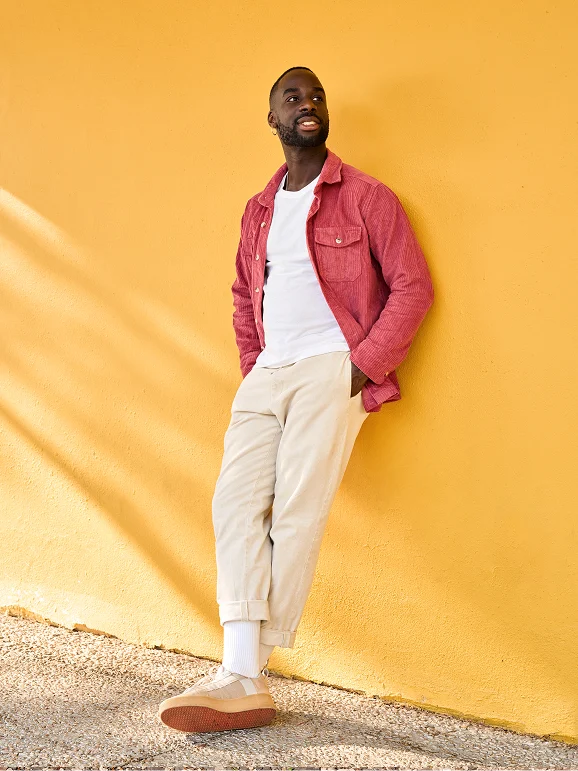 A man wearing a red jacket leans against a yellow wall