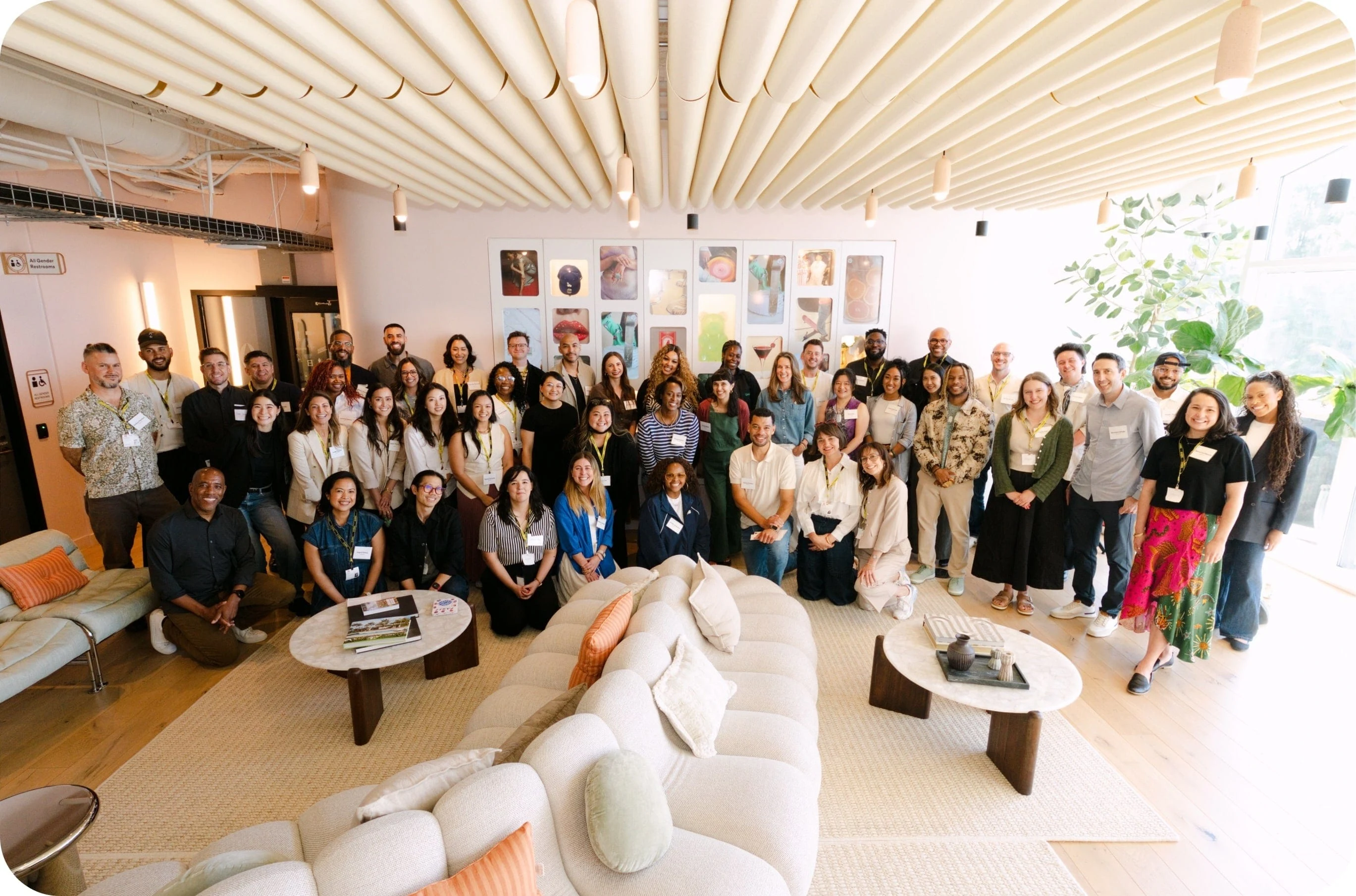 A large group of people posing together in a bright, modern lounge area with couches, coffee tables, and artwork on the wall.