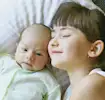Une petite fille tenant tendrement son nouveau bébé frère ou sœur, illustrant le moment de la présentation familiale.