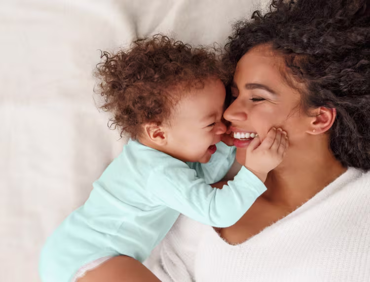 Mother and baby dressed in light blue laying down smiling at each other