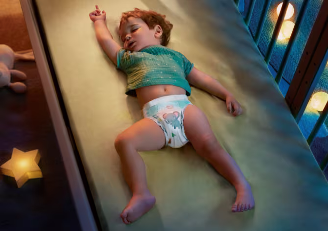 Ein schlafendes Baby liegt in einem Babybettchen und trägt eine Pampers Baby-Dry Windel.