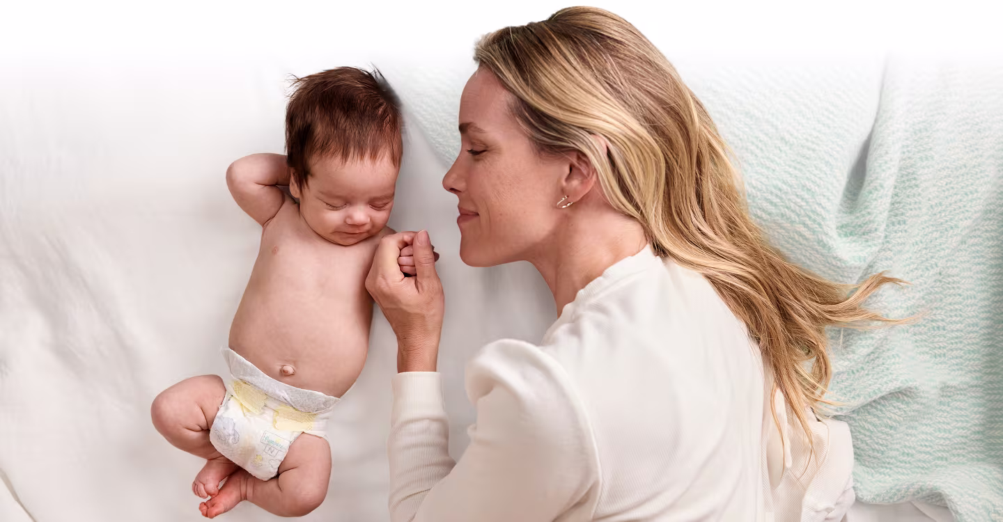 A mother gently cradles her sleeping newborn, their cheeks touching in a tender embrace.