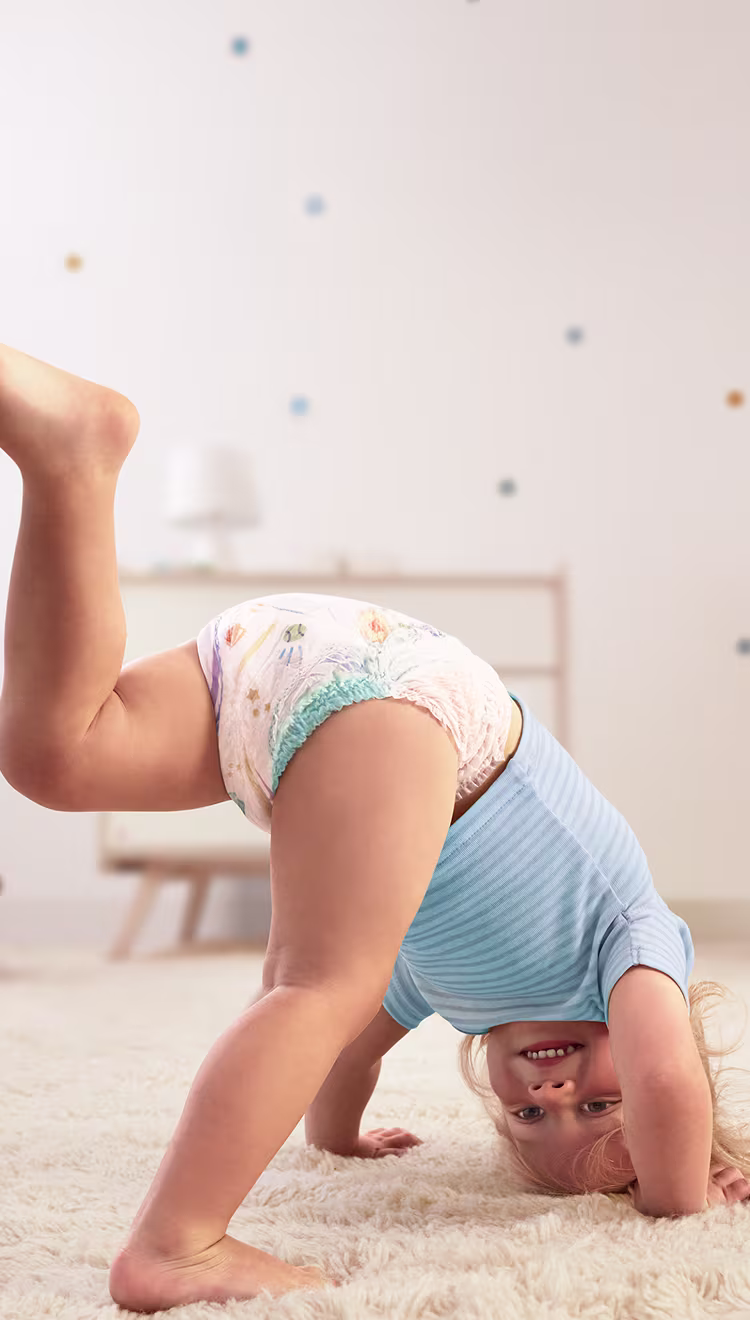 Een baby die een Pampers® Baby-Dry™ Pants draagt, doet een handstand en steekt één been in de lucht.