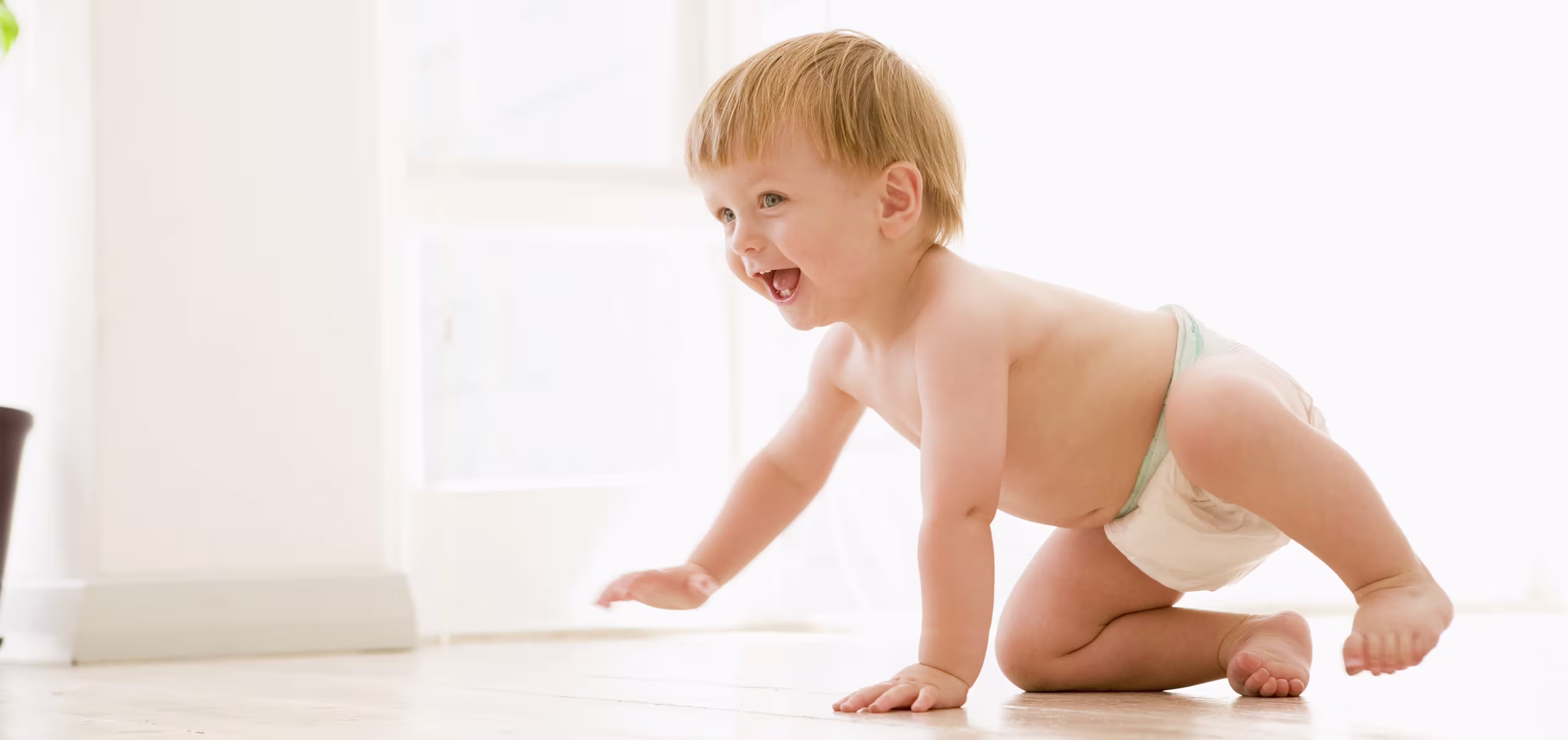Bebé sonriente jugando cómodamente en pañales, representando la protección de la piel y el confort diario que ofrece Pampers