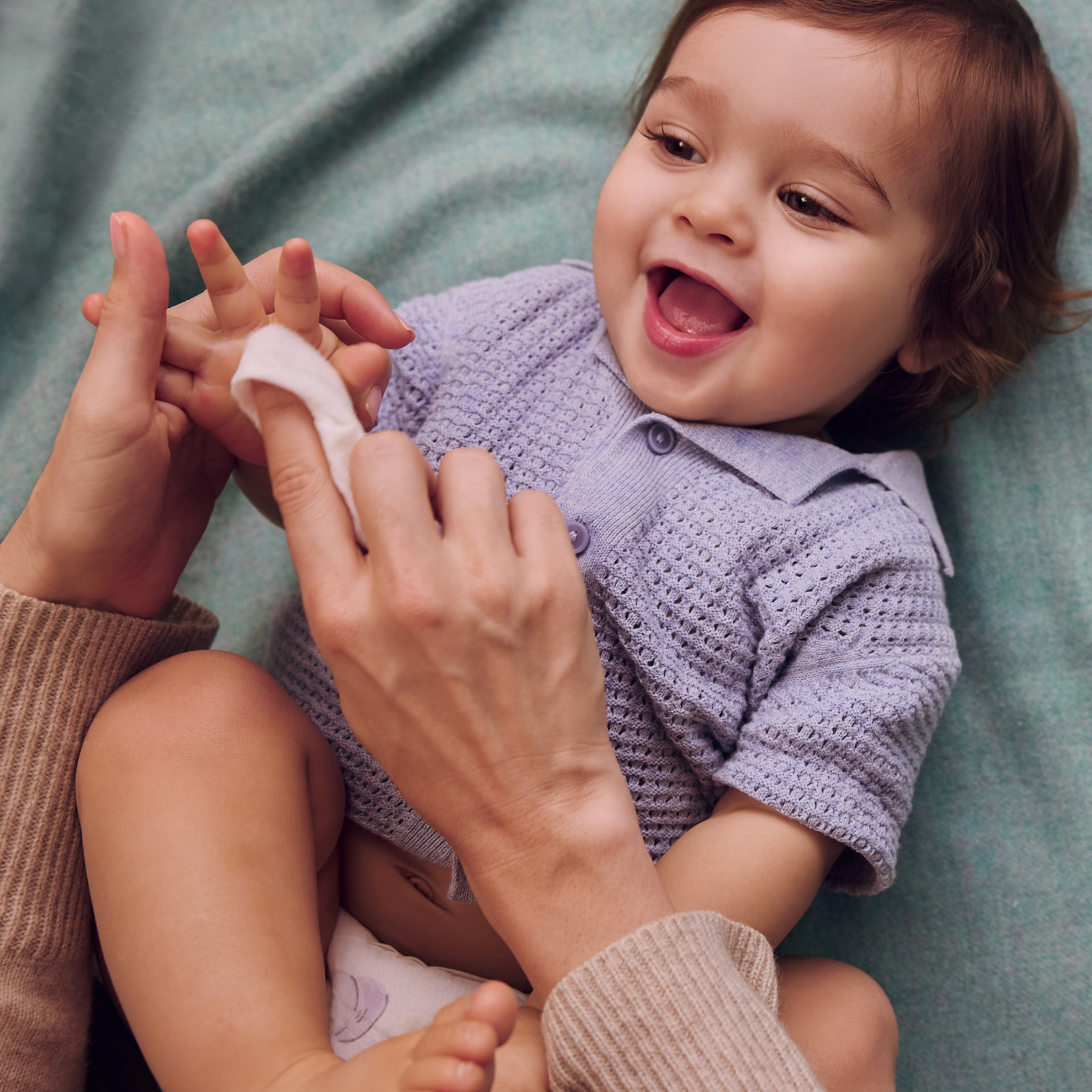 Mom cleaning her smiling baby’s hand with a Pampers aqua pure wipe Mom cleaning her smiling baby’s hand with a Pampers aqua pure wipe