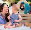 Smiling woman and baby in matching blue outfits celebrating first birthday with a teddy bear and colorful "ONE" sign.