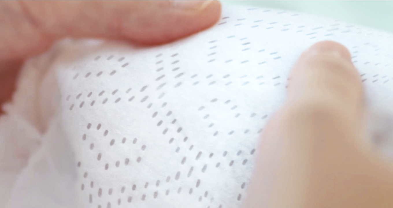 Nahaufnahme zweier Daumen, die das Innenvlies eine Pampers Premium Protection Windeln anfassen. Dank der Millionen von Mikroporen hält es Urin und flüssigen Stuhl von der Babyhaut fern.