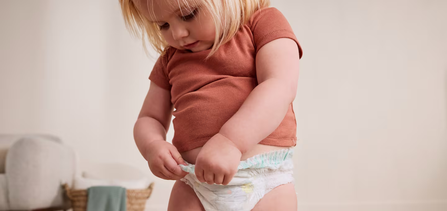 Toddler looking down while adjusting their diaper, showing independence and early self-care.