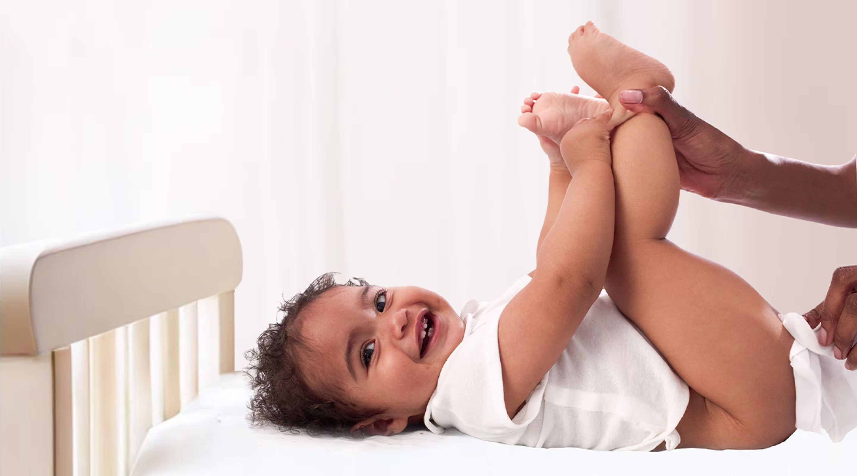 Un bebé está tumbado de espaldas sobre una superficie blanca, levantando los pies mientras un padre utiliza una toallita para limpiar el trasero del bebé.