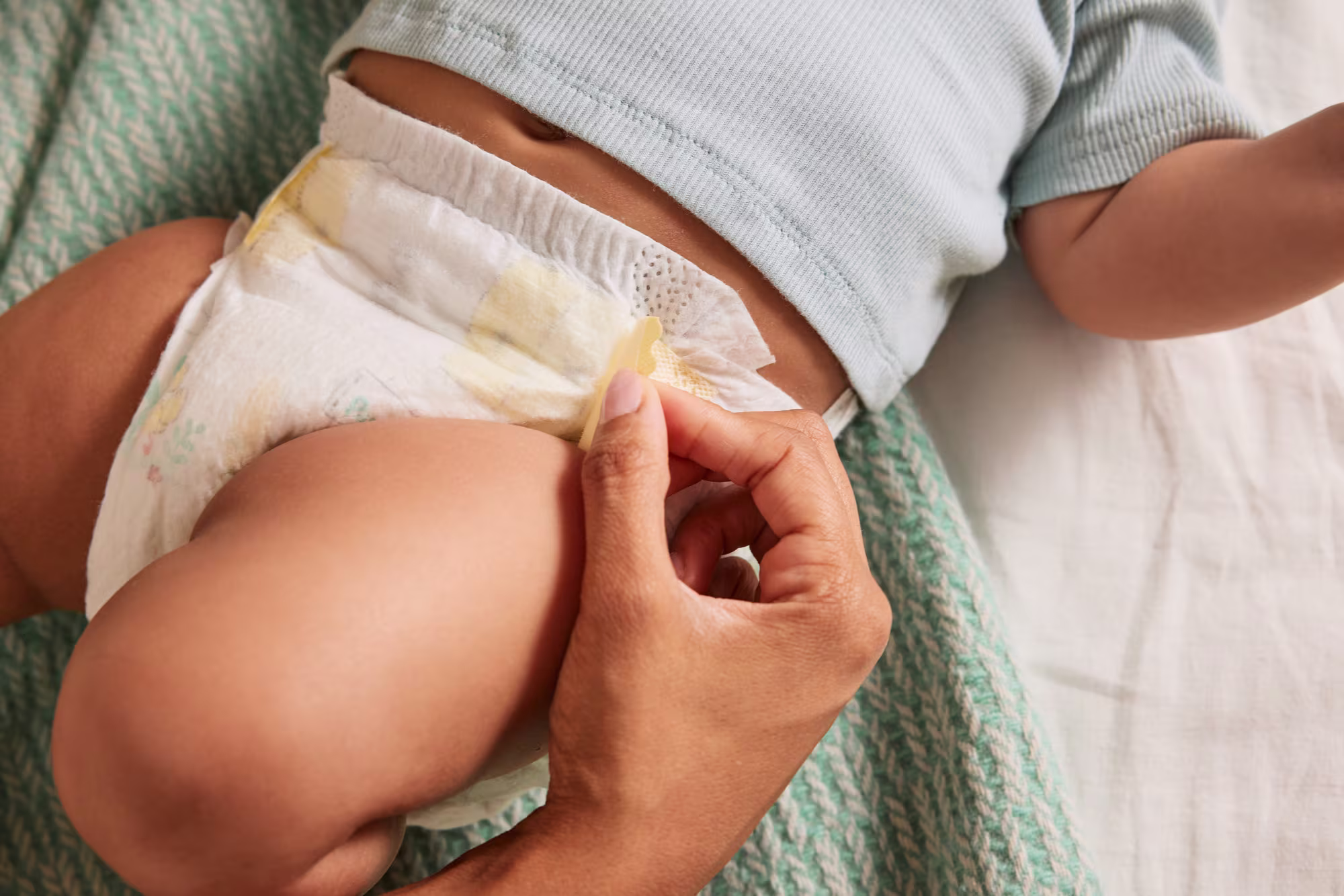Lächelndes Baby liegt auf einer weißen Unterlage, während ein Erwachsener die Windel wechselt.