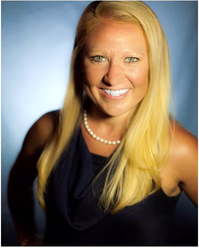 A female scientist with blonde hair and blue eyes and long straight hair smiles.