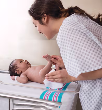 Uma nova mãe está a mudar a fralda do seu recém-nascido e a limpar o rabinho do bebé com uma toalhita num quarto do hospital.
